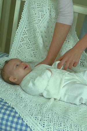Baby on a knitted blanket wearing a white cardigan